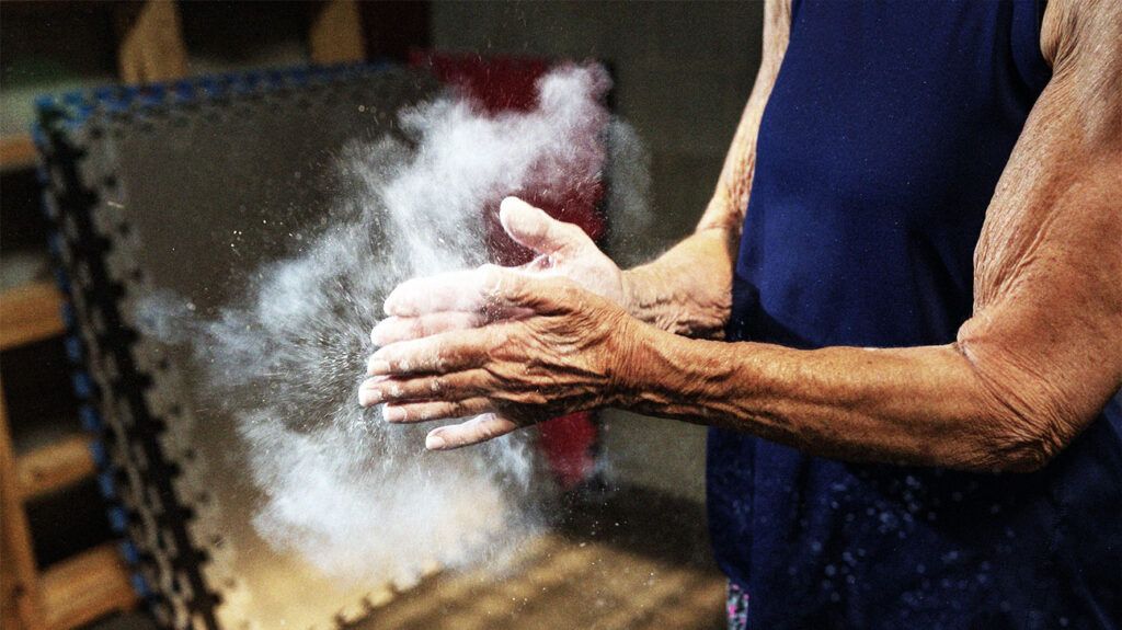 Zbliżenie starszej osoby w stroju sportowym pocierającej dłonie, podczas gdy wokół niej tworzy się chmura kredy 